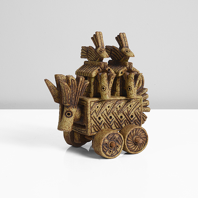 Stoneware ceramic, dry ochre and brown glazes, the rectangular form with a drawer mounted with an antelope head, the top inset with two removable huts with creatures, raised on four wheels made by Ian Godfrey